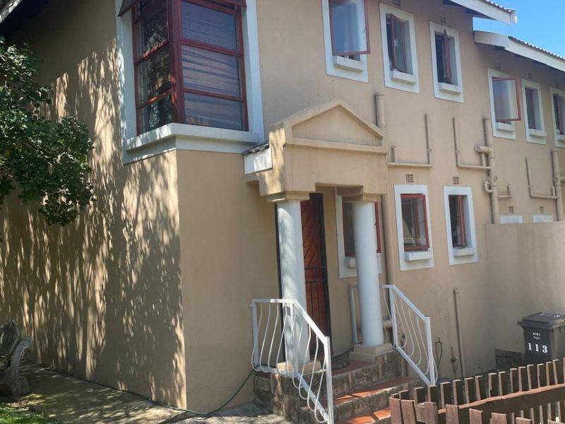 Front elevation of a two-story residential property featuring a paved driveway, covered entrance with decorative columns, and casement windows.