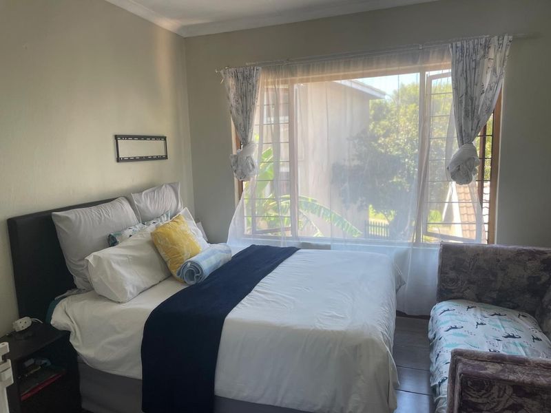 A cozy bedroom featuring laminate flooring, a large window with security bars, and coved ceiling details, offering a comfortable and functional living space.