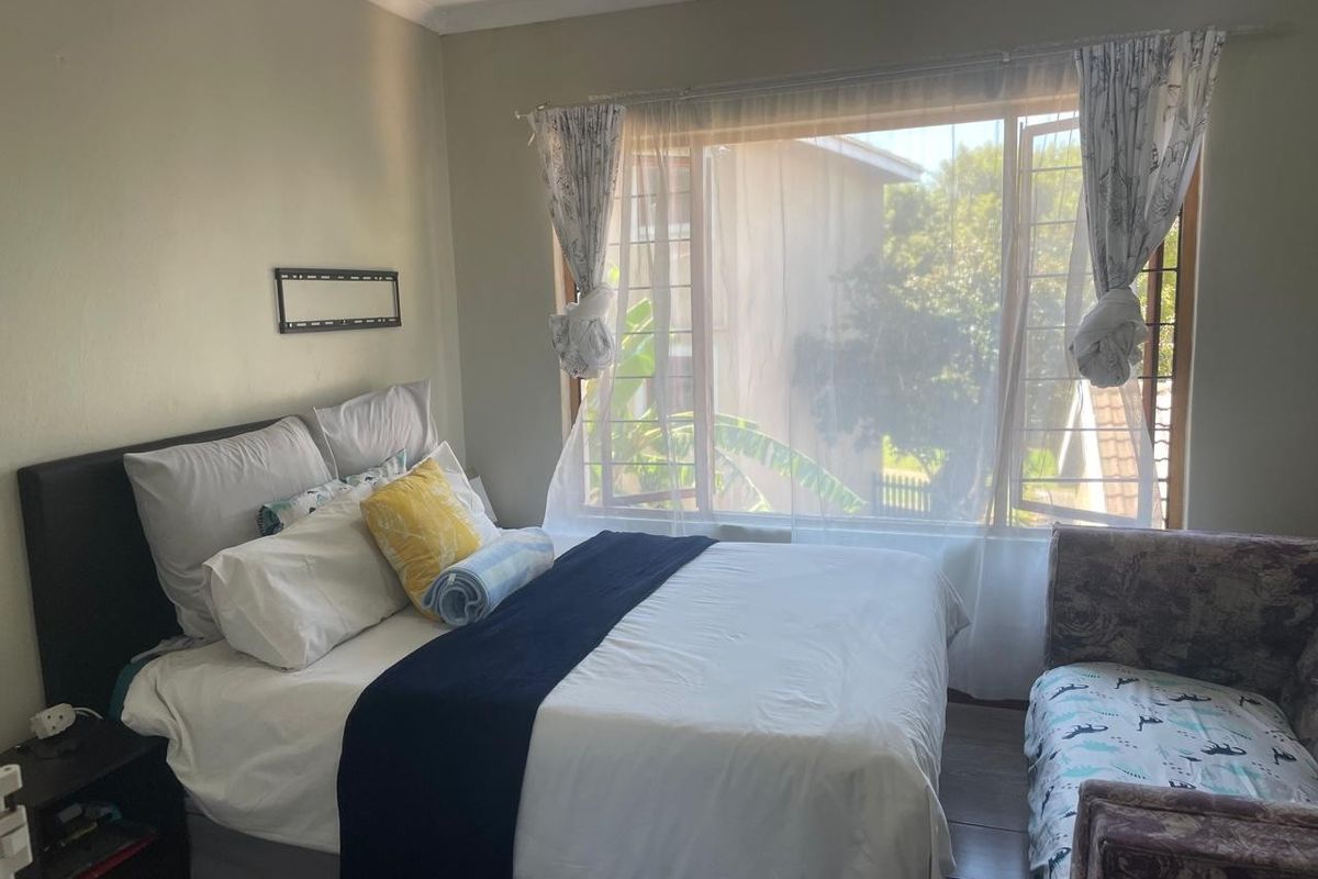 A cozy bedroom featuring laminate flooring, a large window with security bars, and coved ceiling details, offering a comfortable and functional living space.