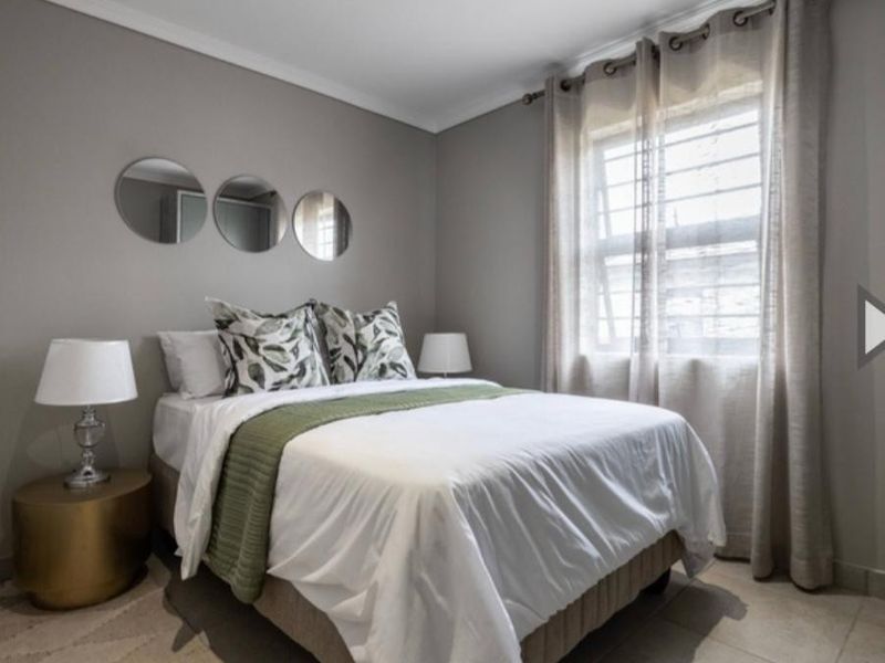 A well-maintained bedroom featuring neutral grey walls, tiled flooring, and a window fitted with security bars.