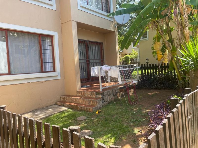 Rear exterior view of the property featuring a small tiled patio, sliding door access, and a private garden area enclosed by a wooden picket fence.