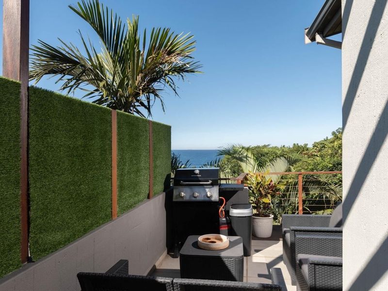 A private balcony featuring a built-in grill, artificial grass privacy screen, and scenic ocean views.
