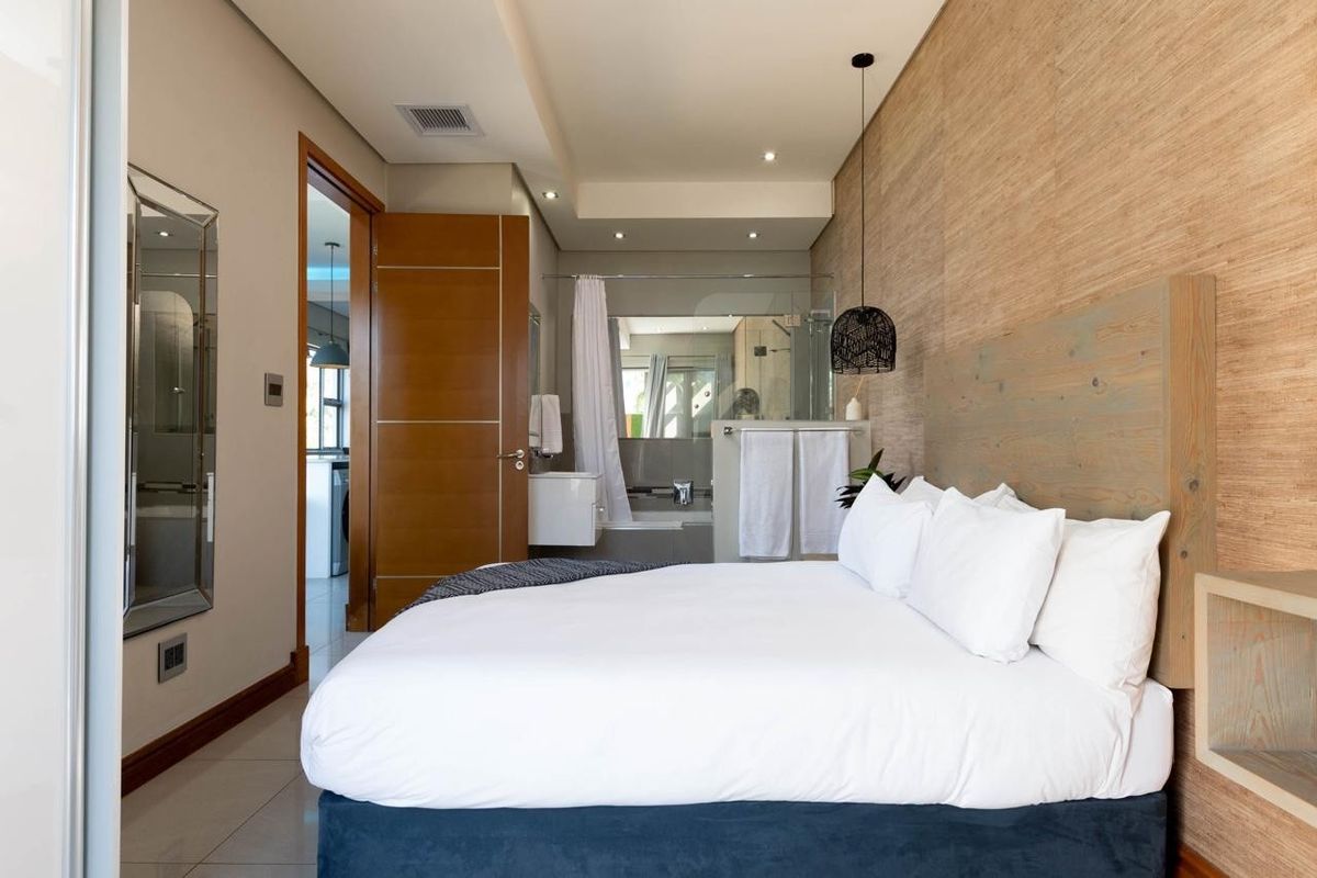 Modern bedroom featuring timber-look wall paneling, recessed ceiling lighting, and an integrated en-suite bathroom with high-quality finishes.