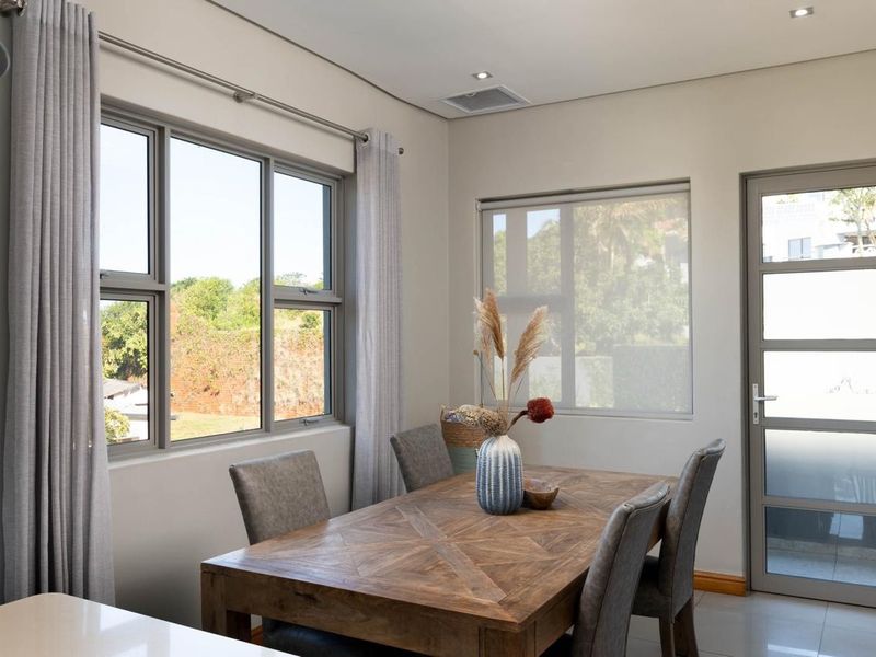 A bright and modern dining area featuring tiled flooring, recessed downlighting, and large aluminium-framed windows that provide ample natural light.