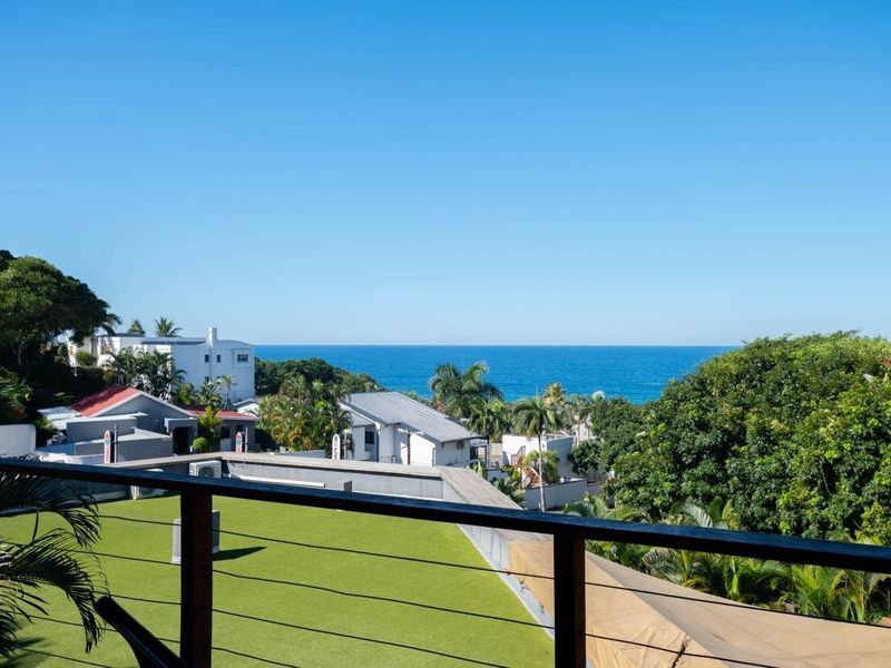 A scenic elevated view overlooking the surrounding coastal neighborhood and the ocean, featuring a balcony with a modern railing and artificial turf.