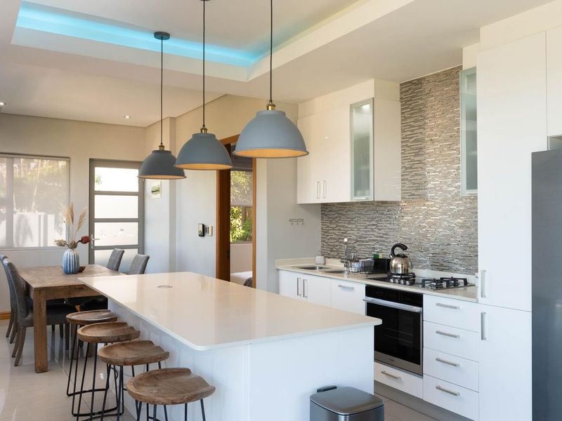 Modern open-plan kitchen featuring a central island with quartz countertops, high-gloss cabinetry, integrated appliances, and stylish pendant lighting, seamlessly flowing into the dining area.