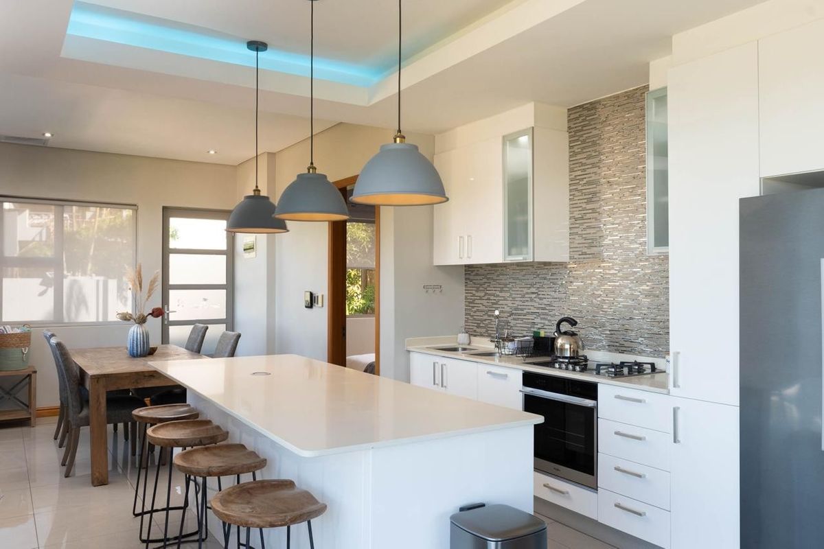 Modern open-plan kitchen featuring a central island with quartz countertops, high-gloss cabinetry, integrated appliances, and stylish pendant lighting, seamlessly flowing into the dining area.