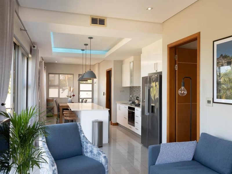 Modern open-plan living area featuring a sleek kitchen with a central island, tiled floors, and recessed ceiling lighting, creating a bright and functional space.