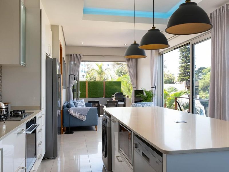 Modern open-plan kitchen and living area featuring a central island, high-end built-in appliances, sleek cabinetry, and large sliding doors leading to a balcony.