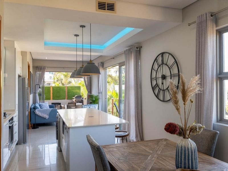 Modern open-plan living and kitchen area featuring a central island, stone countertops, recessed ceiling lighting, and seamless access to an outdoor patio.