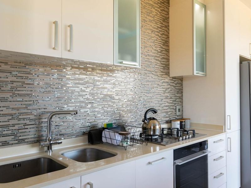 Modern kitchen featuring sleek white cabinetry, stone countertops, a mosaic tile backsplash, and integrated stainless steel appliances.