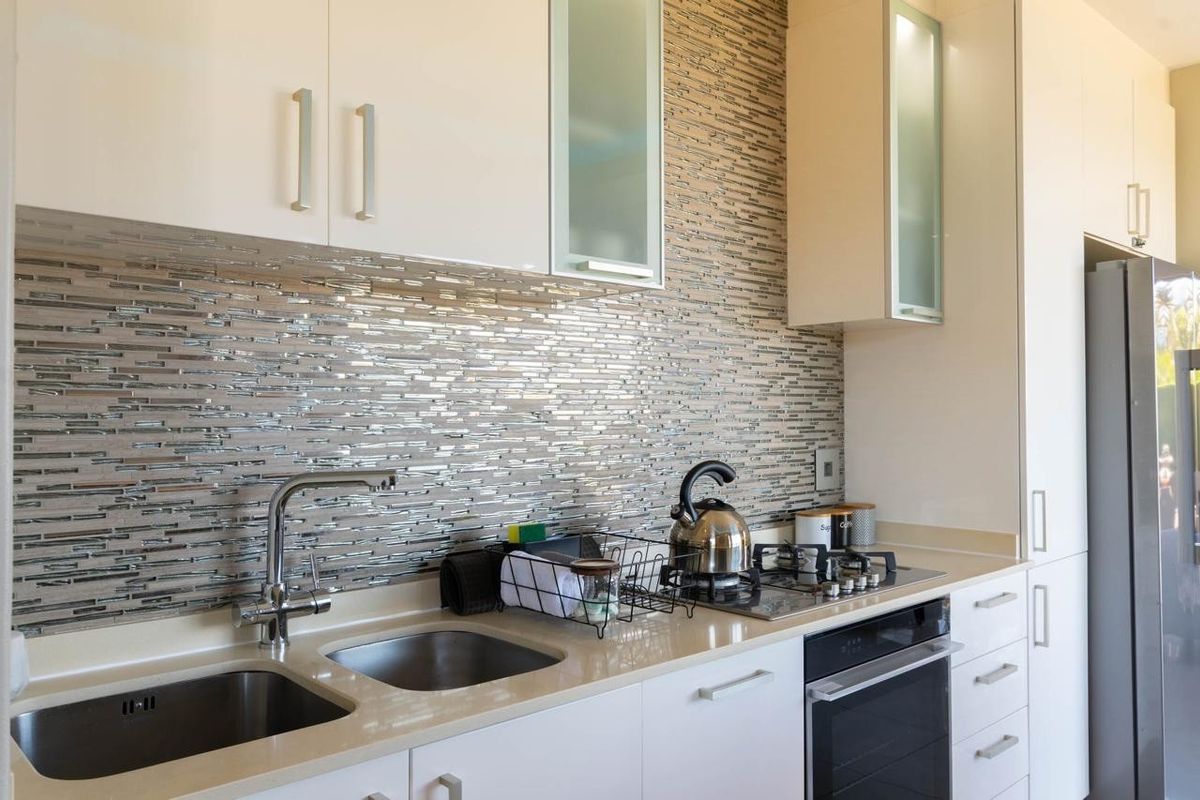 Modern kitchen featuring sleek white cabinetry, stone countertops, a mosaic tile backsplash, and integrated stainless steel appliances.