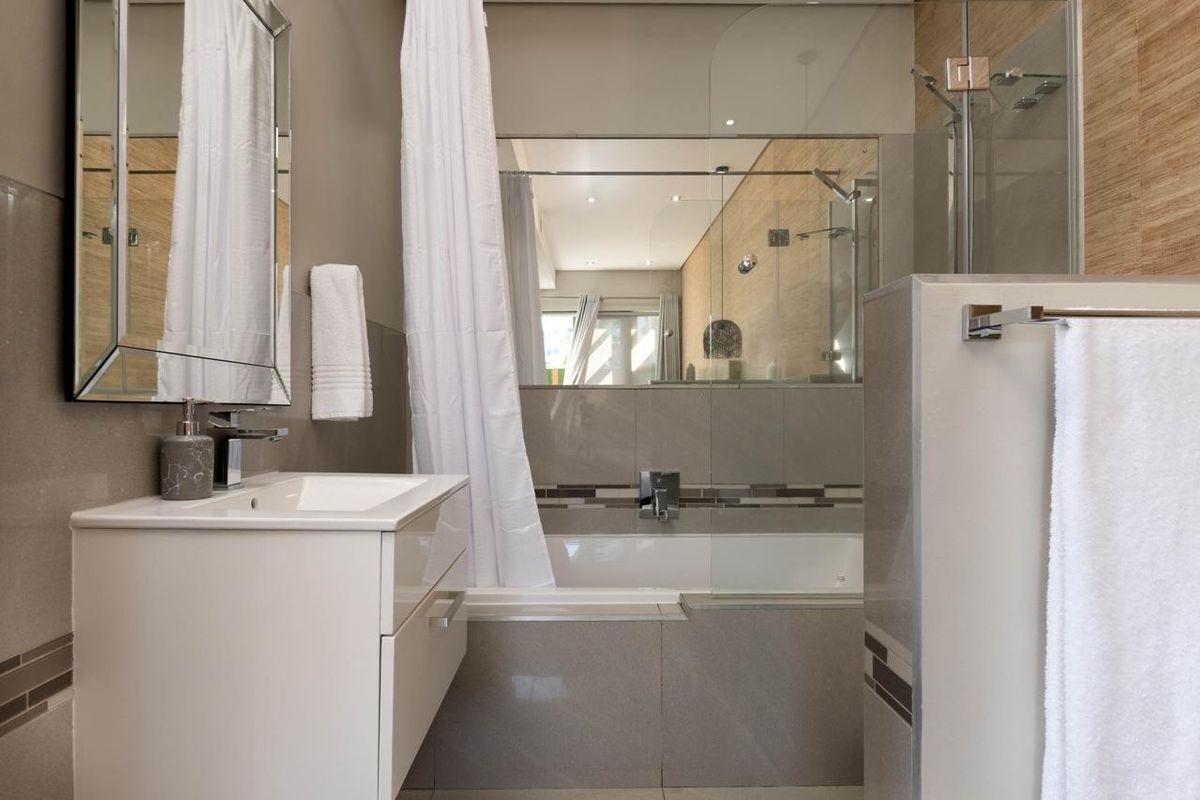 Modern bathroom featuring a vanity with basin, a bathtub with a glass shower screen, and contemporary wall tiling.