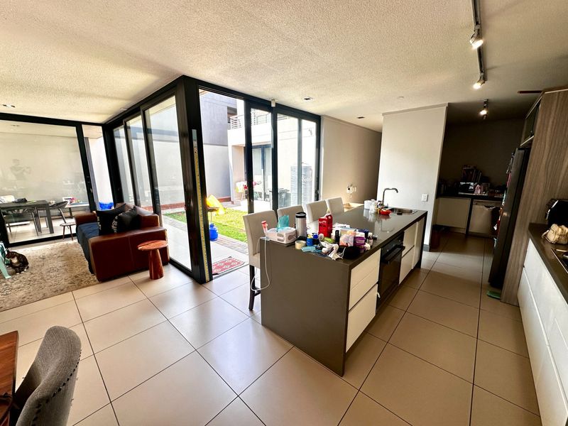 Modern open-plan living area featuring a central kitchen island with built-in oven and seamless access to the rear patio through large glass sliding doors.