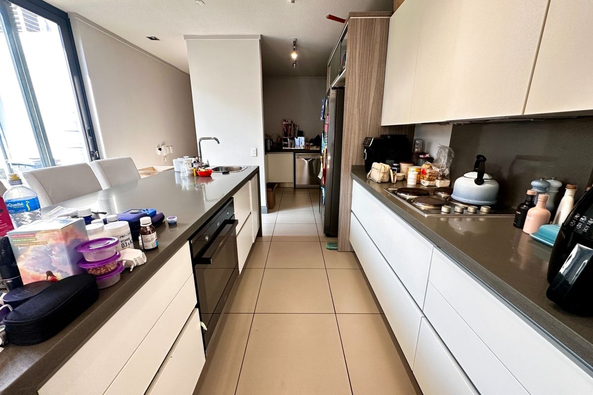 Modern galley-style kitchen featuring sleek handleless cabinetry, stone countertops, integrated appliances, and large format floor tiles.