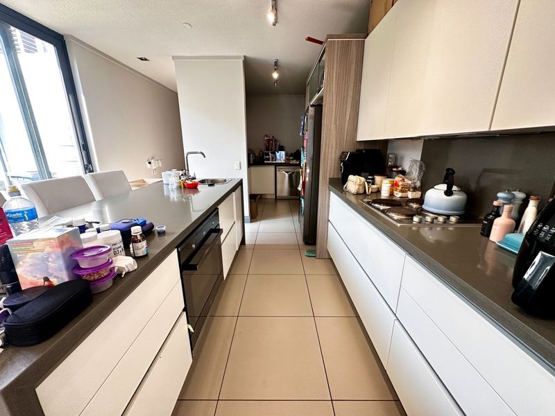 Modern galley-style kitchen featuring sleek handleless cabinetry, stone countertops, integrated appliances, and large format floor tiles.