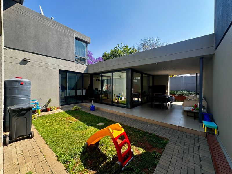 A modern rear exterior featuring a covered patio with tiled flooring, large sliding glass doors, and a landscaped garden area with paved pathways.
