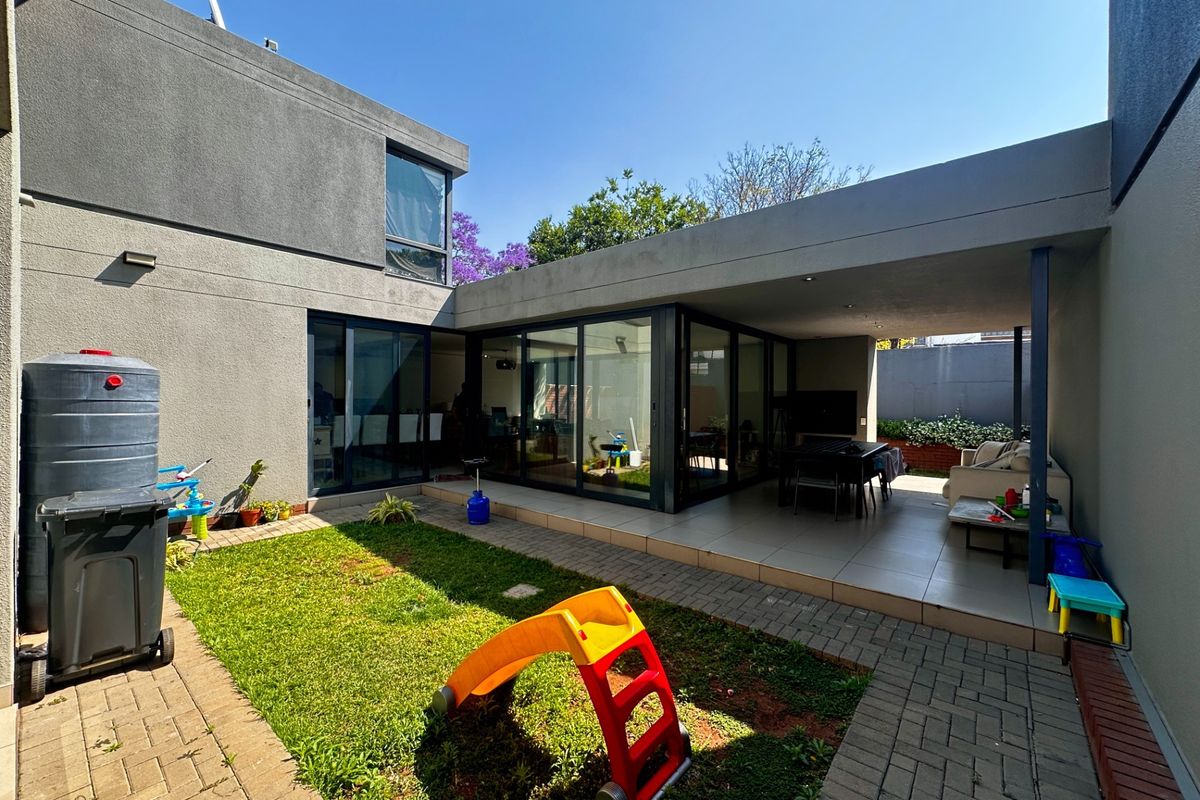 A modern rear exterior featuring a covered patio with tiled flooring, large sliding glass doors, and a landscaped garden area with paved pathways.