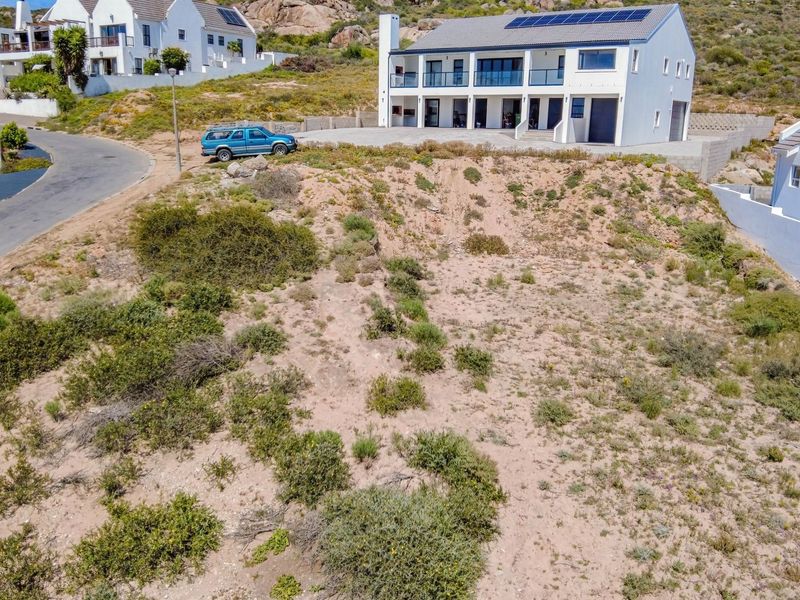 An elevated aerial view of a vacant residential plot featuring sloped terrain, situated in a developed coastal neighborhood.
