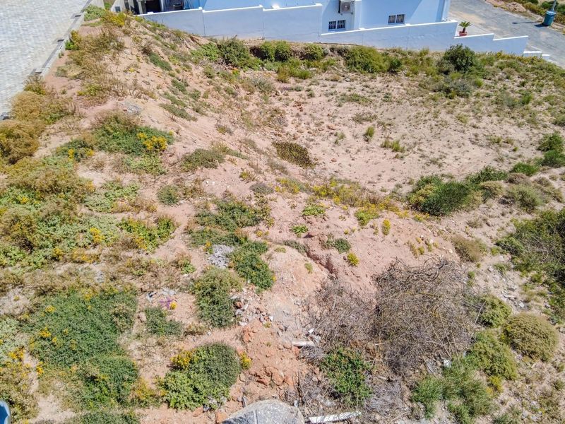 An aerial view of a vacant residential plot featuring sloped terrain and natural vegetation, ready for development.