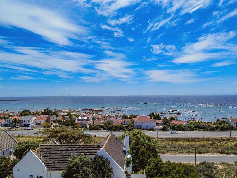 An aerial view of a coastal residential area featuring a clear ocean horizon and surrounding neighborhood infrastructure.