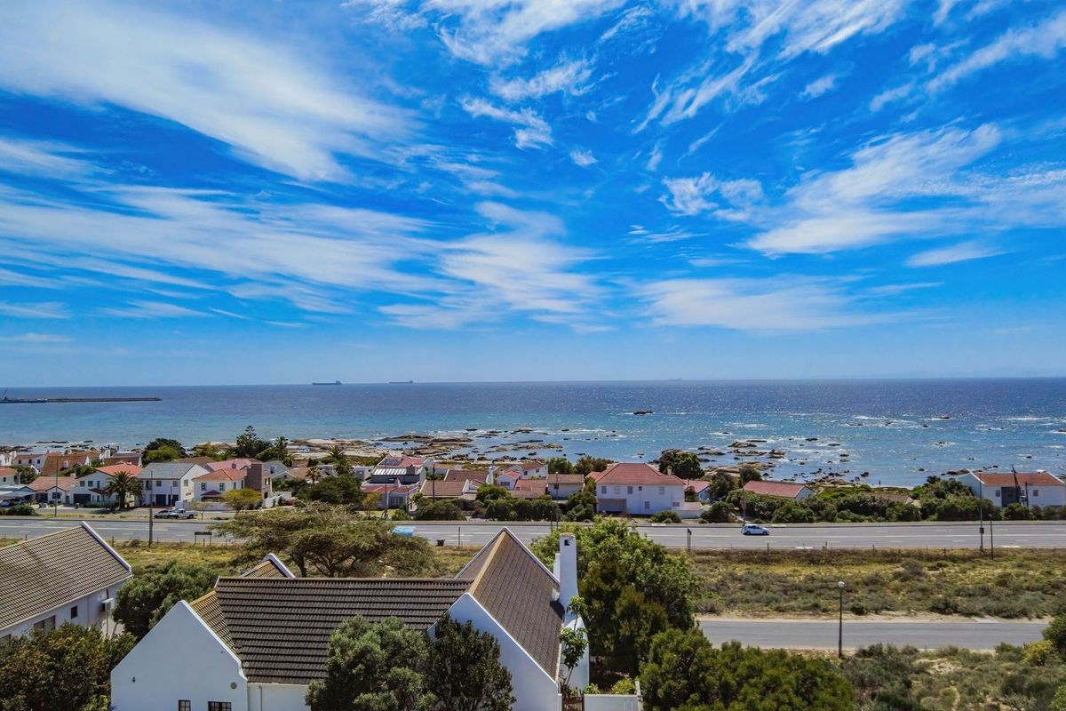 An aerial view of a coastal residential area featuring a clear ocean horizon and surrounding neighborhood infrastructure.