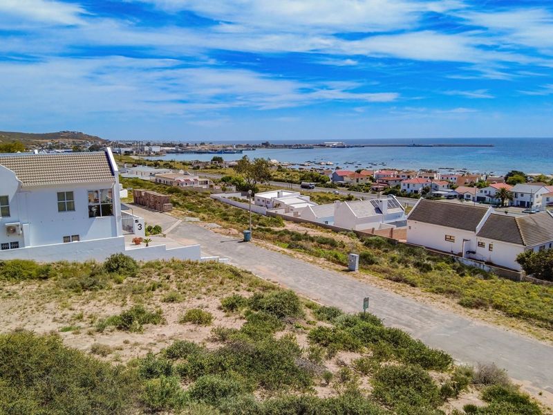 An elevated aerial view of a residential area featuring a paved road, surrounding homes, and a scenic coastal outlook.