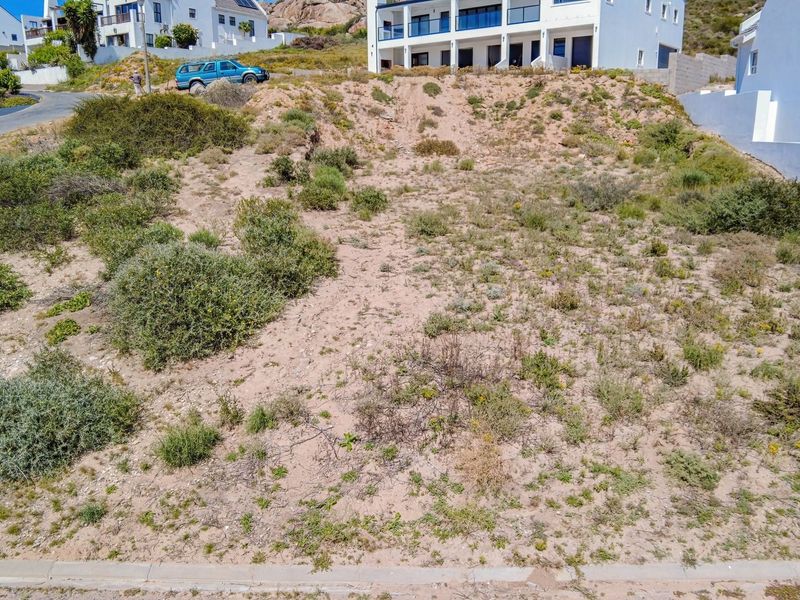 A vacant residential plot featuring a sloped terrain, situated in a developed neighbourhood with established surrounding properties.