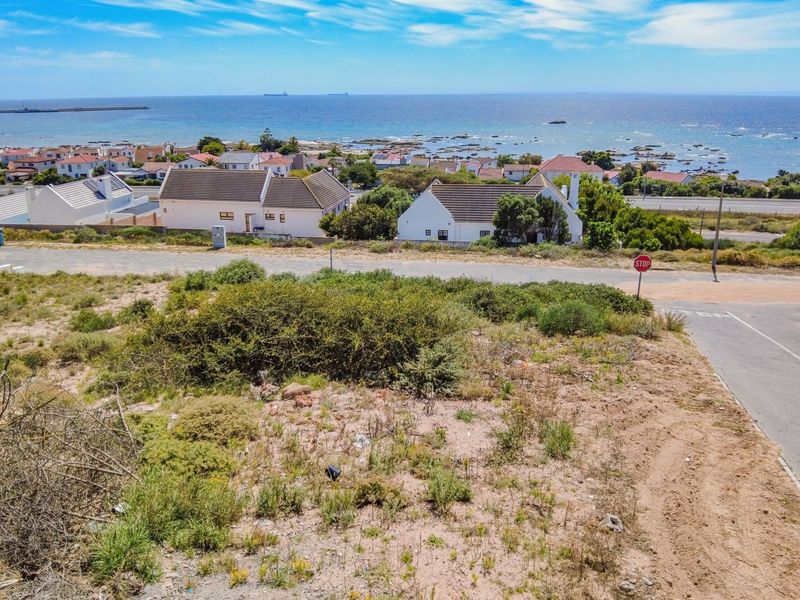 An aerial view of a vacant residential plot featuring coastal views and direct access to a paved street.