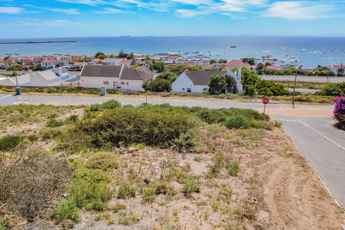 An aerial view of a vacant residential plot featuring coastal views and direct access to a paved street.