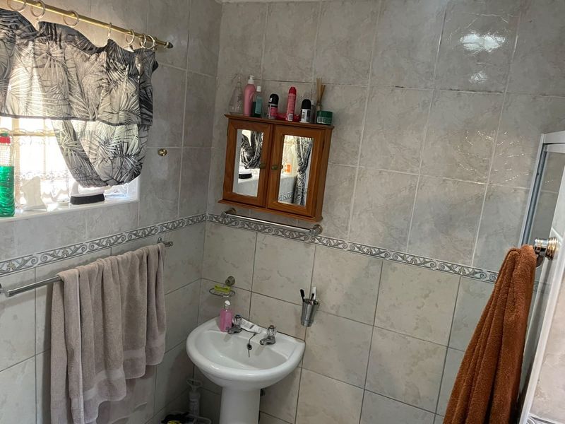 A functional bathroom featuring tiled walls, a pedestal basin, and a wall-mounted medicine cabinet, offering a clean and practical space.