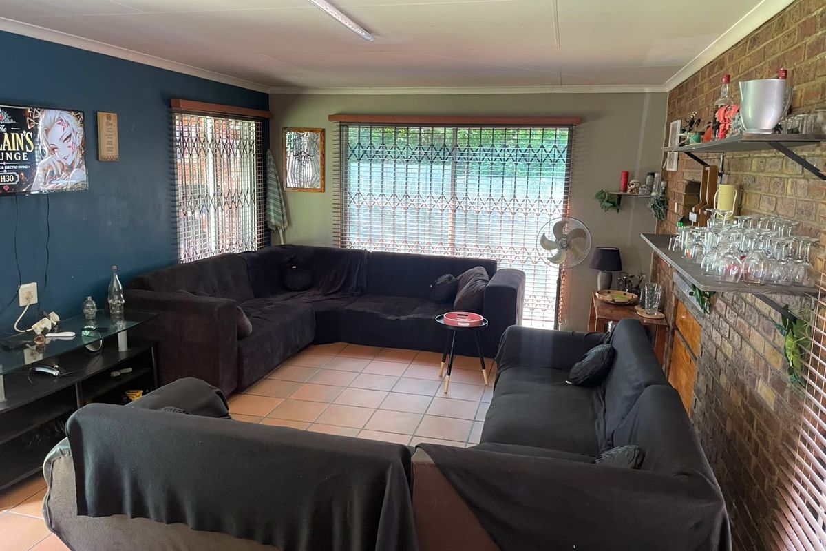Spacious living room featuring an exposed brick feature wall, ceramic tiled flooring, and large windows with security gates.