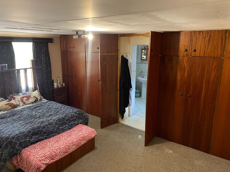 Bedroom featuring extensive built-in wooden cabinetry and direct access to an en-suite bathroom, requiring cosmetic updates to the ceiling and flooring.