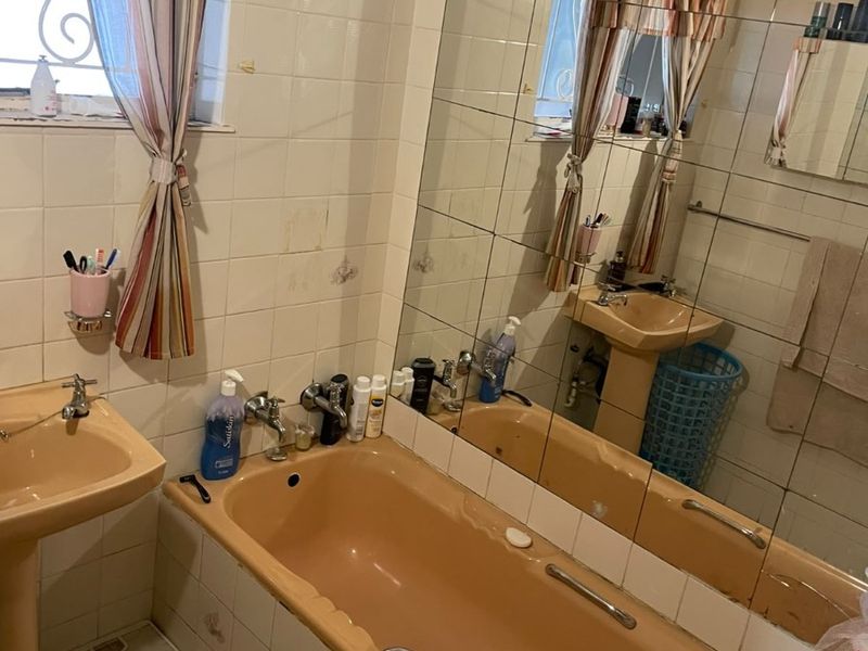 A dated bathroom featuring a peach-colored pedestal basin and matching bathtub, complemented by wall-to-wall tiling and a large vanity mirror.