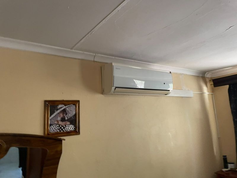 A bedroom interior featuring a wall-mounted air conditioning unit, showing visible signs of ceiling cracking and wall surface wear.