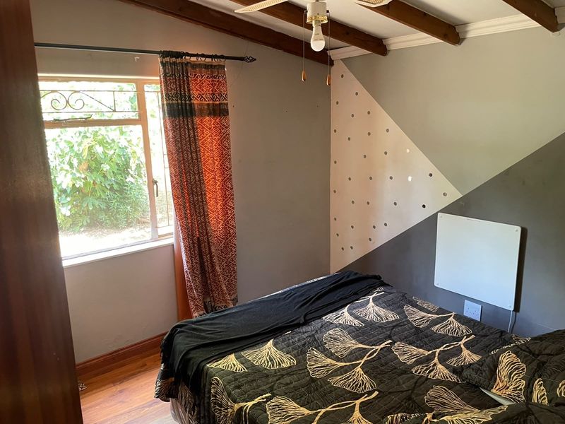A bedroom featuring exposed timber ceiling beams, a ceiling fan, laminate flooring, and a wall-mounted electric heater.