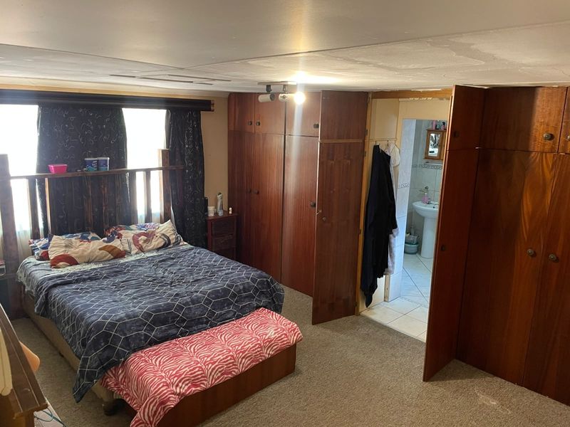 Bedroom featuring built-in wooden cupboards and an attached en-suite bathroom with a pedestal basin. The room requires cosmetic updates to the ceiling and flooring.