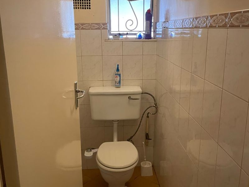 A compact bathroom featuring ceramic wall and floor tiles, a standard toilet, and a wall-mounted light fixture.