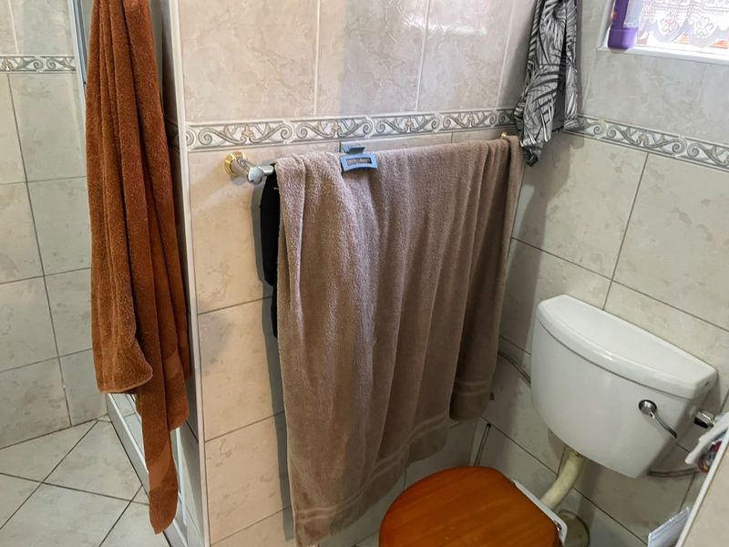 A functional bathroom featuring ceramic wall and floor tiling, a standard toilet, and a shower enclosure.