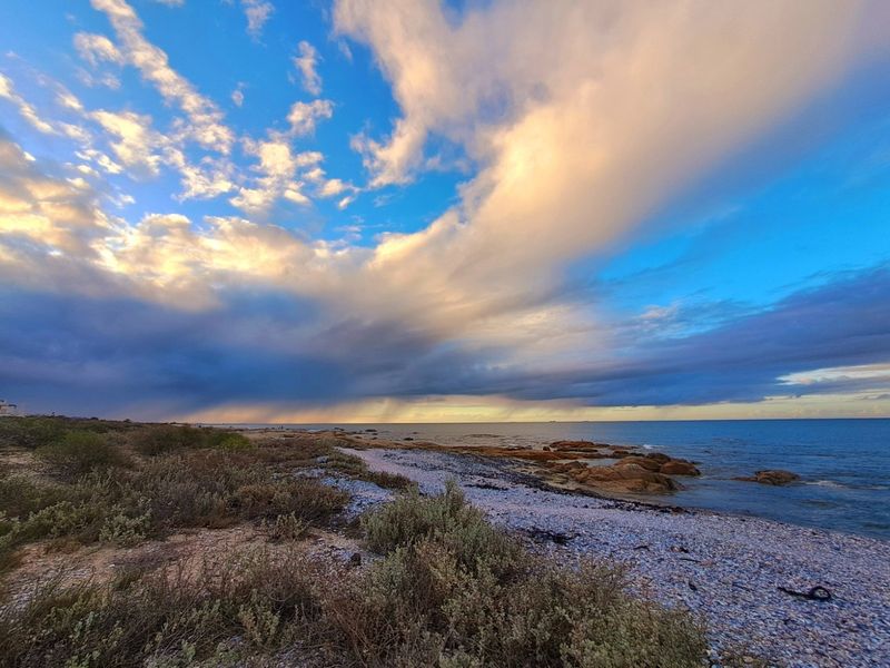 A scenic view of the natural coastal shoreline featuring rocky outcrops and native vegetation under a dramatic cloudy sky.