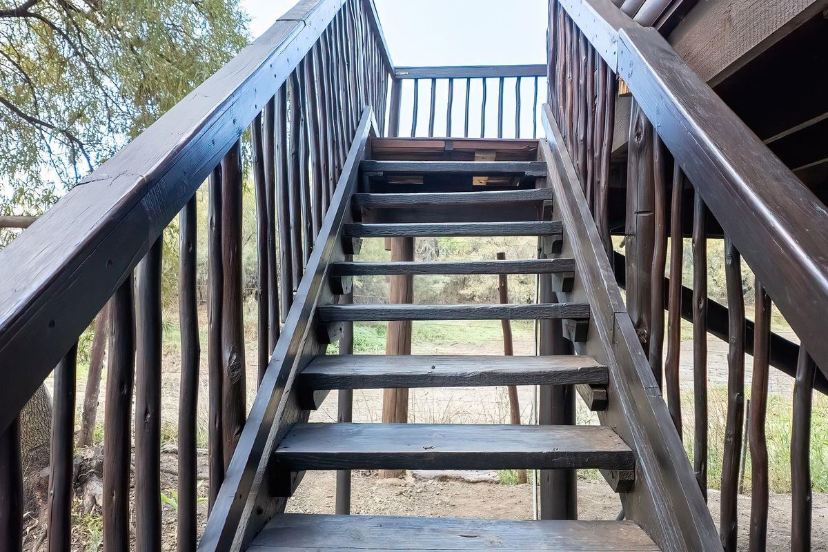 An outdoor timber staircase leading to a raised deck area, featuring rustic wooden railings and structural supports in a natural farm setting.