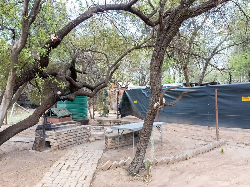 Outdoor entertainment area featuring a built-in brick braai, paved walkway, and integrated seating area set within a natural, tree-shaded farm garden environment.