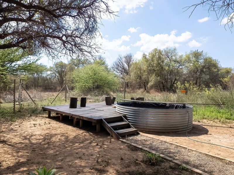 A rustic outdoor plunge pool area featuring a corrugated metal tank set into a timber deck, surrounded by natural bushveld landscape.