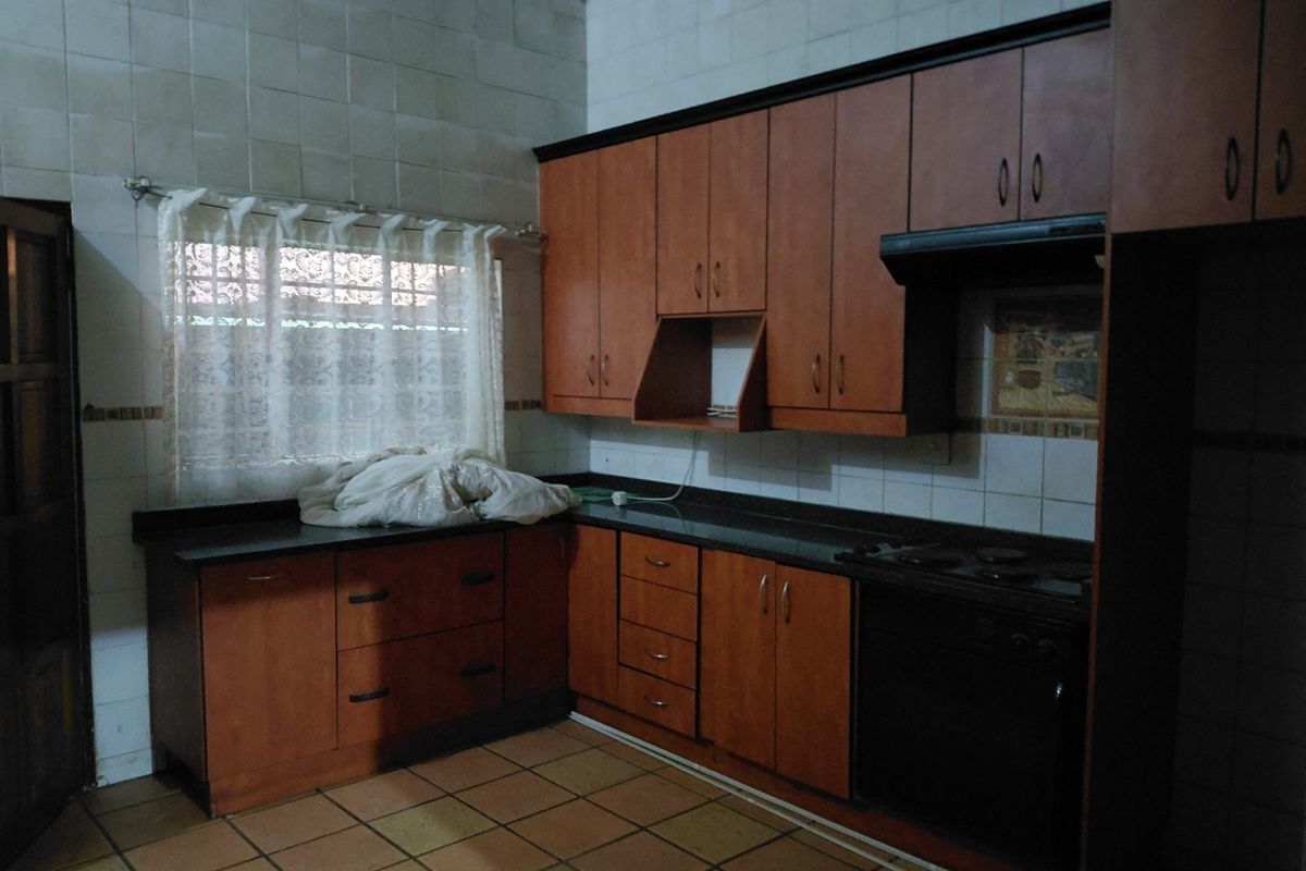 A functional kitchen featuring wooden cabinetry, granite countertops, built-in oven, and hob, with tiled splashbacks and flooring throughout.