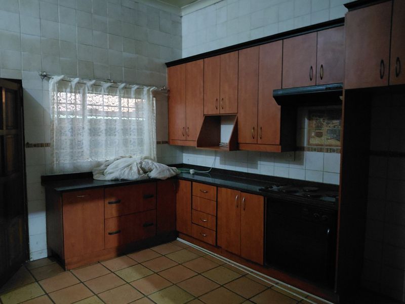 A functional kitchen featuring wooden cabinetry, granite countertops, built-in oven, and hob, with tiled splashbacks and flooring throughout.