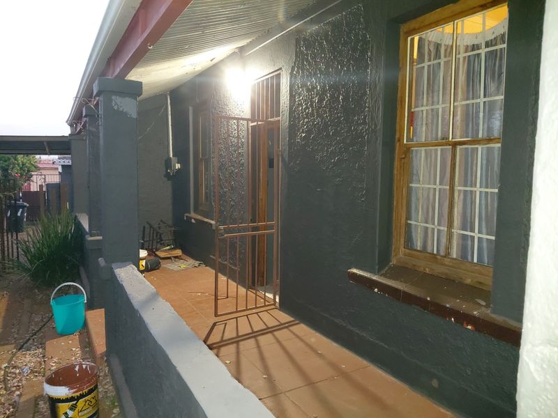 A covered front veranda featuring tiled flooring, security gate, and timber-framed windows, providing a functional entrance area for the home.
