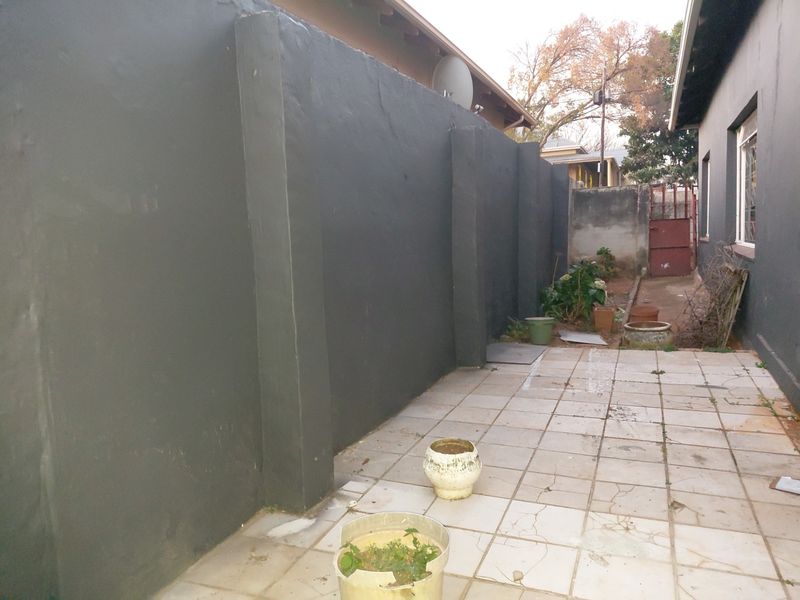A side exterior area featuring a paved patio and a high perimeter wall, providing a private outdoor space.