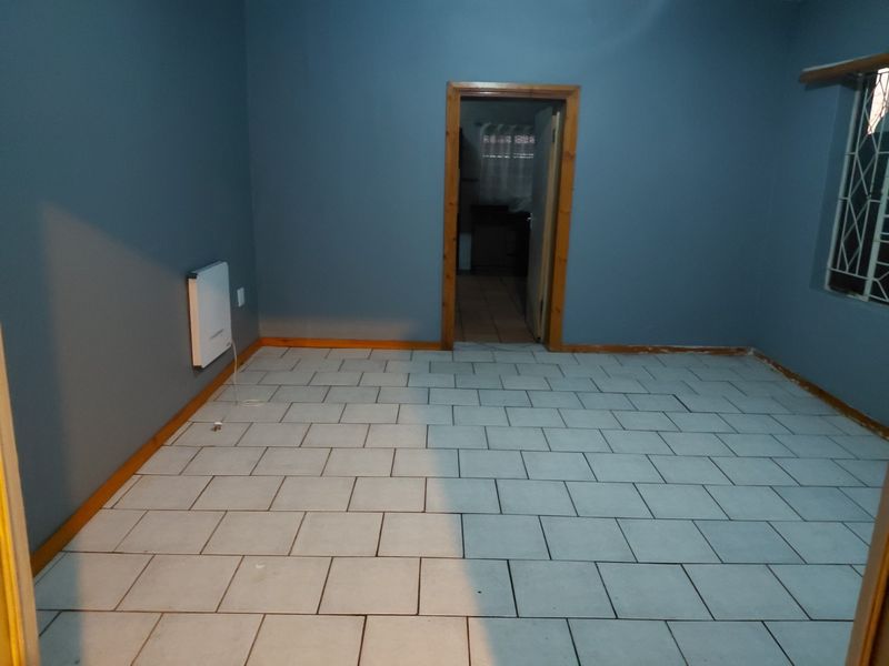 An empty living room featuring ceramic tile flooring, wooden skirting boards, and a wall-mounted electric heater, providing a blank canvas for interior design.