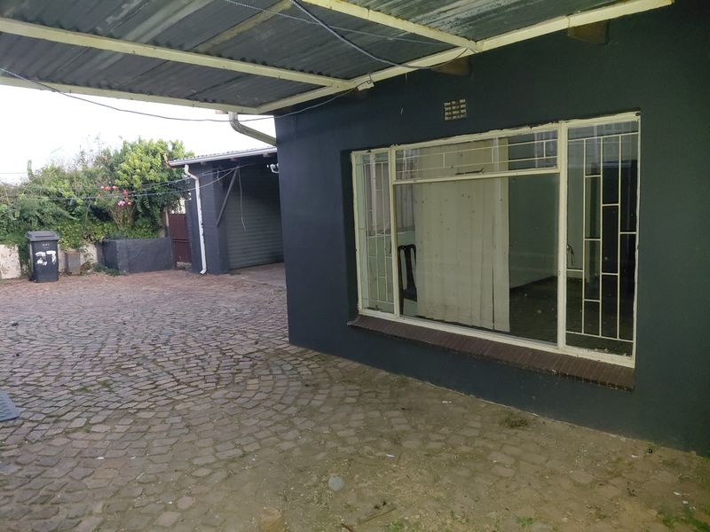 Front exterior view featuring a covered carport, cobblestone driveway, and dark painted facade with security-barred windows.
