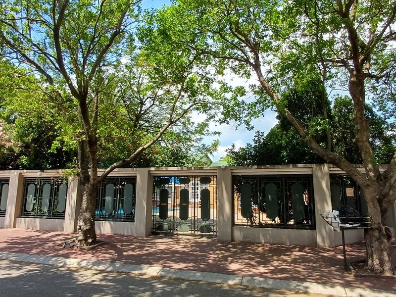 Front view of the property featuring a secure perimeter wall with decorative wrought iron gates and mature trees along the sidewalk.